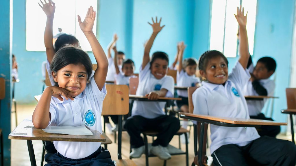 Niños del programa Mi Nueva Familia levantando la mano en un salón de clase