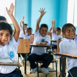 Niños del programa Mi Nueva Familia levantando la mano en un salón de clase